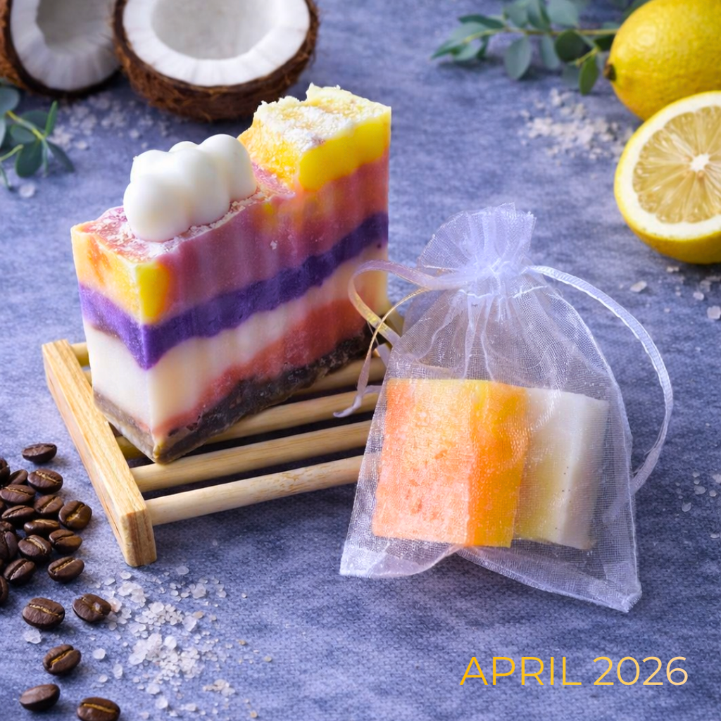 Colorful layered soap bars with a transparent bag, coconuts, lemons, and coffee beans on a blue surface.