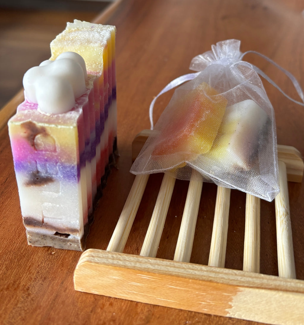Colorful soap bar with a tooth-shaped object on top, next to a white drawstring bag with more soap bars inside, on a wooden surface.